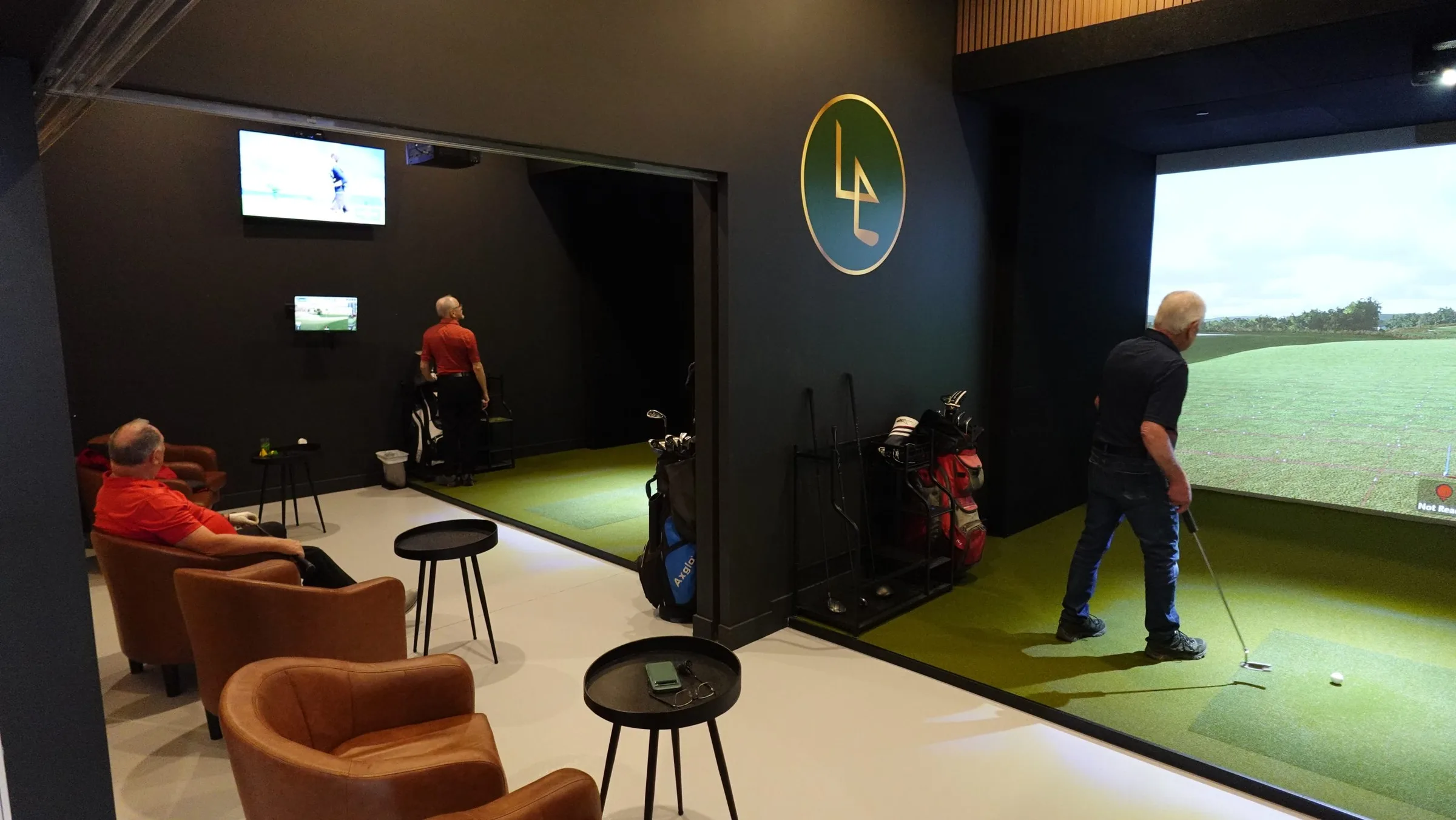 Une salle privée du Foursome : fauteuils de cuir, deux golfeurs à l’écran.